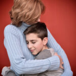 Happy and smiling young boy with closed eyes hugging his lovely mother