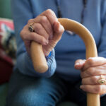 Close Up Of Senior Woman Sitting In Chair Holding Walking Cane
